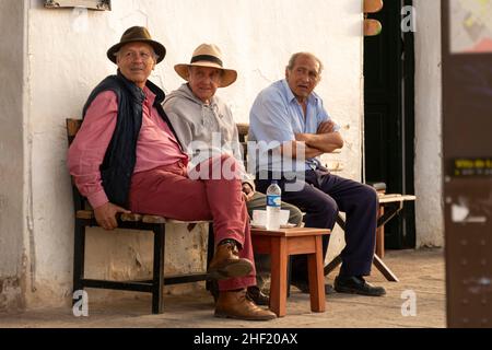 Drei Männer saßen entspannt auf der kolonialen Plaza Mayor de Villa de Leyva, Boyacá, Kolumbien. Die Welt an sich vorbei beobachten. Stockfoto