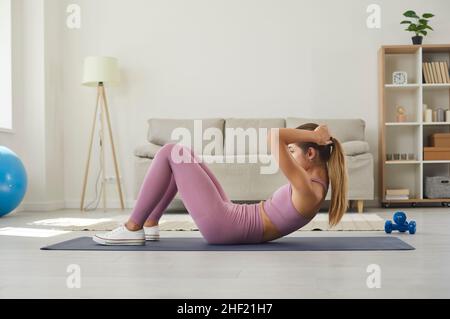 Fit junge Frau tut Sit-ups oder knirscht auf Trainingsmatte während des Sport-Training zu Hause Stockfoto