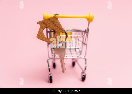 Nahaufnahme des Schlüssels mit einem Schlüsselanhänger in Mini-Pushcart auf einem rosa Hintergrund. Konzept von Leasing, Hypothek und Kauf von Immobilien. Stockfoto