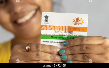 Birbhum, Westbengalen / Indien - 21st. Dezember 2021: Selektiver Fokus auf die Aadhaar-Karte, die von einer jungen Inderin mit lächelndem Gesicht in der Hand gehalten wird Stockfoto