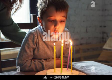 Kleiner kaukasischer Junge im Vorschulalter, der zu Hause Kerzen auf dem hausgemachten Geburtstagskuchen ausbläst, das Kind wünscht sich während der Geburtstagsfeier mit der Familie. Selecti Stockfoto