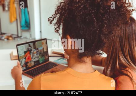 Rückansicht von zwei Freundinnen zu Hause Blick auf Laptop-Bildschirm, multirassische Freundinnen Surfen Internet Scrollen Social Media auf dem Computer, während Sie verbringen Stockfoto