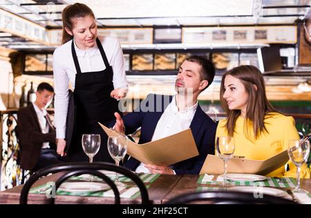 Die Kellnerin nimmt die Bestellung von einem Paar, das zu Abend gegessen hat, an Stockfoto