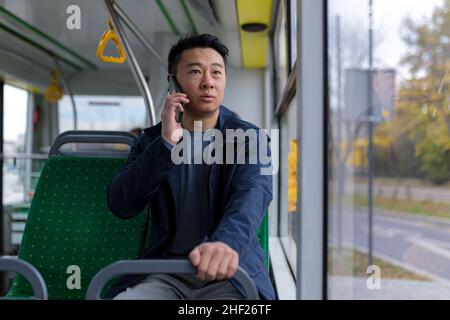 Ängstlicher und verängstigter asiatischer Mann, der in einem öffentlichen Bus fährt, ein Passagier, der auf einem Mobiltelefon spricht Stockfoto