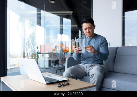 Ängstlich asiatische versuchen, Online-Zahlung per Kreditkarte und Telefon, Geschäftsmann arbeiten im Büro, Bank-Antrag Fehler zu machen Stockfoto