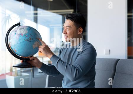Asiatische männliche Blogger Tourist, Blick auf Kamera und lächelnd halten Globus, Verkäufer von touristischen Touren, lädt zum Reisen Stockfoto