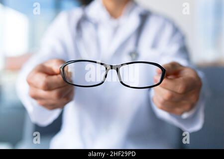 Nahaufnahme der Hände des Arztes, der eine Brille hält, bietet der Augenarzt dem Patienten eine Brille an Stockfoto