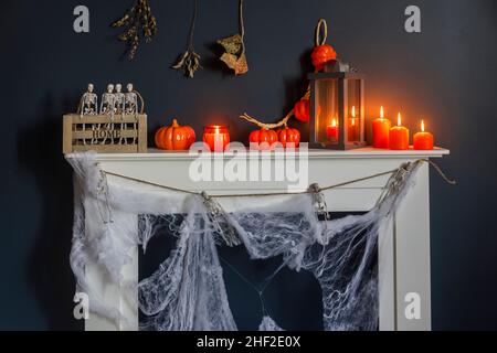 Halloween-Heimtextilien. Plastikspielzeug-Skelette in einer Holzkiste am Kamin vor einer dunkelblauen Wand. Eine Girlande aus Skeletten. Spinnennetz auf den dres Stockfoto