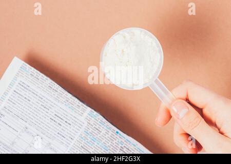 Schaufel Proteinpulver in der Hand der Frau neben der Packung Produkt auf braunem Tisch, Draufsicht Stockfoto