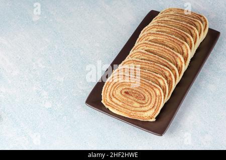 Geschnittenes Bolo de rolo auf einem braunen Teller und einem blau-weißen Hintergrund. Stockfoto