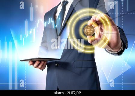 Geschäftsmann hält eine Tablette mit steigenden Kryptowährungsdaten und zeigt mit seiner Hand eine Bitcoin-Münze. Investitionen in virtuelle Währungen Stockfoto