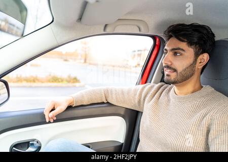 Mann im Pullover sitzt auf dem Beifahrersitz und fährt tagsüber im Auto Stockfoto