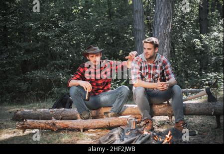 Junge Menschen genießen am Sommertag ein Picknick im Park und trinken Bier. Tourismuskonzept. Picknick-Freunde. Zwei Freunde Holzfäller Arbeiter sitzen in der Stockfoto