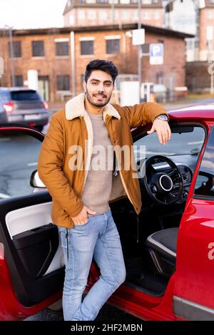 Ein lateinischer oder arabischer Mann lehnte sich neben dem Auto mit geöffneter Tür auf dem Parkplatzplatz der Stadt an Stockfoto