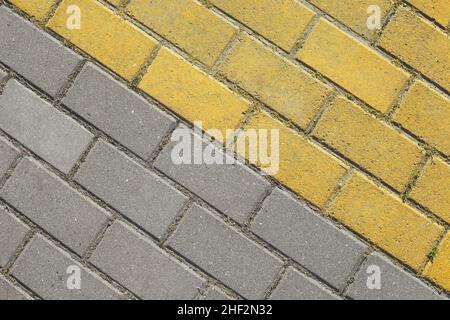 Schräge graue und gelbe Pflasterplatten Draufsicht. Ziegelsteine als Straße, Pflastersteinstruktur. Abstrakt zweifarbige Pflasterstein Hintergrund. Stockfoto