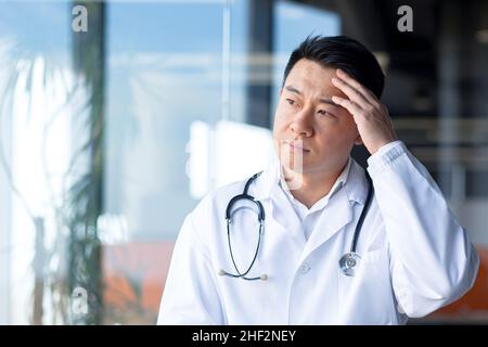 Müde asiatische Arzt, deprimierter Mann in einer modernen Klinik Stockfoto