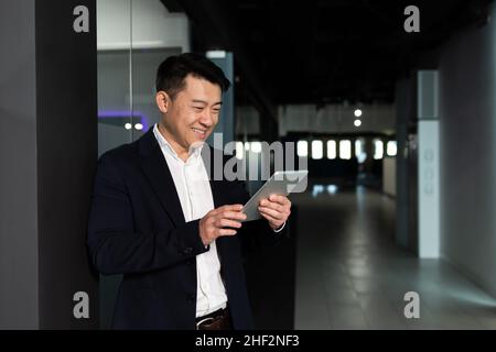 Erfolgreiche asiatische Geschäftsmann Chef Mann, in einem Geschäftsanzug freut und lächelt nutzt einen Tablet-Computer, arbeitet in einem modernen Büro Stockfoto