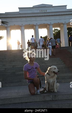 Das junge russische Mädchen genießt ihre Zeit in Sewastopol, der Stadt der russischen Matrosen auf der Krim in der Hafeneinfahrt von Grafskaya Pristan mit ihrem Golden Retriever-Hund Stockfoto