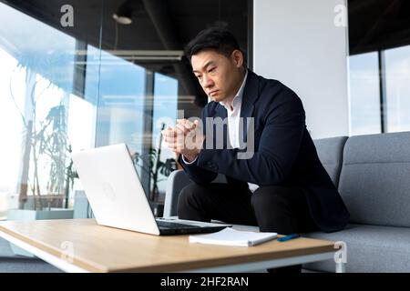 Asiatisch nachdenklicher Geschäftsmann bei Laptop, denken über die Schaffung einer neuen Geschäftsstrategie, erfolgreicher Mann, der im Büro am Laptop arbeitet Stockfoto