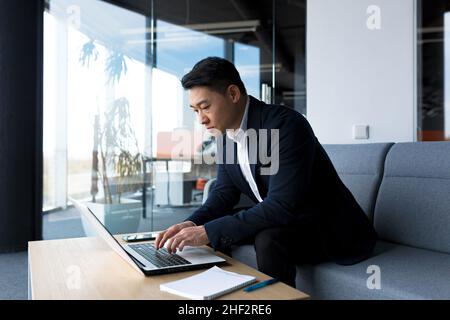 Trauriger Geschäftsmann, der im Büro an einem Laptop arbeitet, frustriert und nachdenklich, gedanklich arbeitet Stockfoto