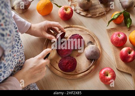 Frau schneidet rote Rübenwurzel - Vorbereitung zum Entsaften von frischem Obst und Gemüse Stockfoto