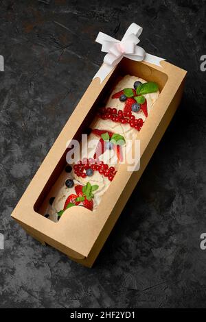 Meringuerolle mit Erdbeeren, Blaubeeren, Himbeeren und Preiselbeeren. Dessert mit frischen Beeren auf einem schwarzen Tisch dekoriert. Stockfoto