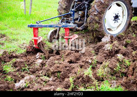 Der Traktor pflügt das Land im Garten mit einem Pflug im frühen Frühjahr. Vorbereitung des Bodens für die Pflanzung von Pflanzen. Stockfoto