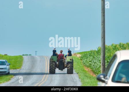 Jugendliche mit Amish Boy und Girl, die an einem Sommertag auf einem alten Traktor auf einem Ackerland reiten Stockfoto