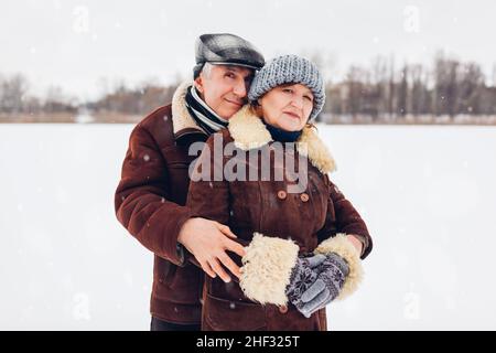 Porträt eines älteren Familienpaares, das während des verschneiten Winterwetters im Freien läuft. Reife Menschen umarmen sich in warmer Kleidung. Valentinstag Stockfoto