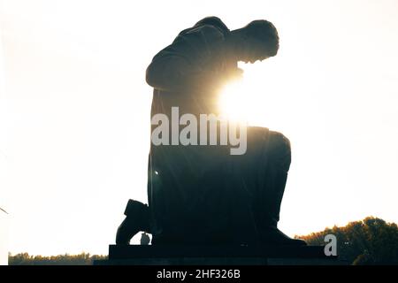 Silhouette einer Statue eines knieenden sowjetischen Soldaten in der Sonne Stockfoto