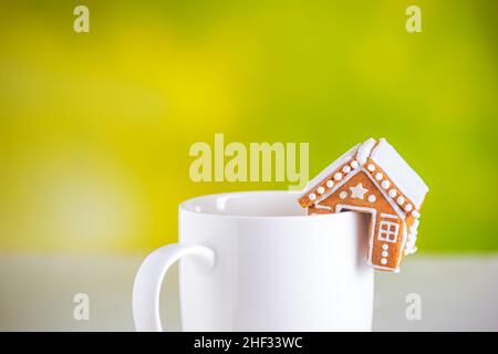 Lebkuchenhütte und eine Tasse Milch mit grünem unscharfem Hintergrund, Nahaufnahme. Weihnachtsfeier Konzept mit Platz für Text Stockfoto