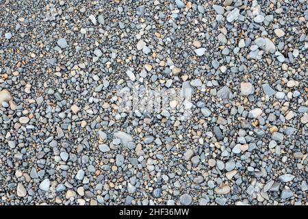 Ein Hintergrund aus kleinen nassen Kieselsteinen in verschiedenen Grau- und Ockertönen. Steine symbolisieren Kraft und Ausdauer. Stockfoto