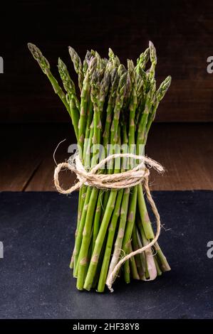Frischer grüner Spargel, gebunden mit einer Schnur auf einem Schiefer und einem rustikalen Holztisch Stockfoto