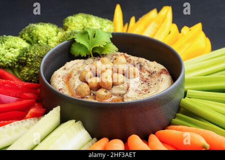 Leckerer Kichererbsen-Hummus in schwarzem Teller mit frischem Gemüse und geräuchertem Paprika Stockfoto