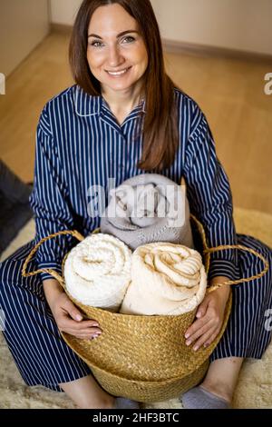 Porträt einer glücklichen jungen Hausfrau in Pyjamas posiert mit Strohkorb für Bettwäsche Lagerung Stockfoto