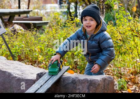 Zwei Jahre alter Junge, der mit einem Spielzeugschlepper auf einer Rampe im Sandkasten des Stadtparks spielt Stockfoto