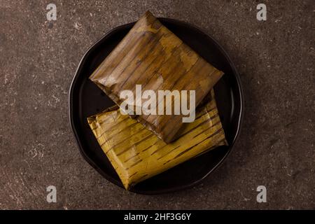 Prähispanische Gericht typisch für Mexiko und einige lateinamerikanische Länder. Maisteig in Bananenblätter gewickelt. Die Tamales werden gedämpft. Stockfoto