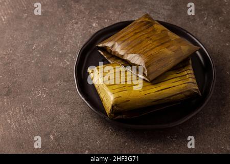 Prähispanische Gericht typisch für Mexiko und einige lateinamerikanische Länder. Maisteig in Bananenblätter gewickelt. Die Tamales werden gedämpft. Stockfoto