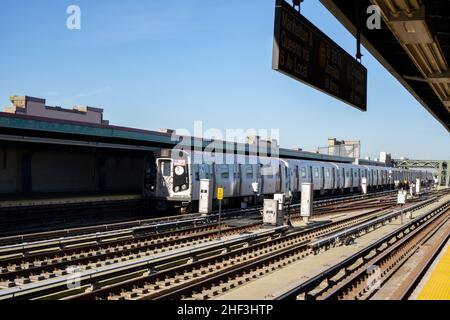 F U-Bahn-Zug nähert sich erhöhten Bahnhof in Brooklyn, New York. Bahngleise auf der Außenplattform Stockfoto