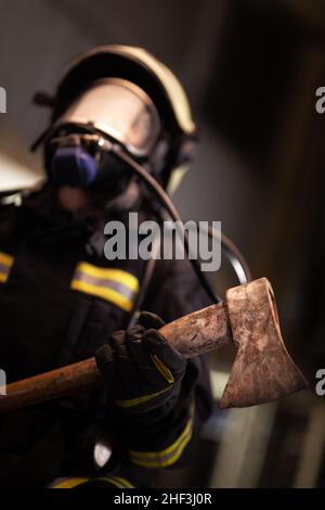 Weibliche Feuerwehrmann Porträt trägt komplette Ausrüstung, Sauerstoff-Maske, und eine Axt. Rauch und Feuer Lastwagen im Hintergrund. Stockfoto