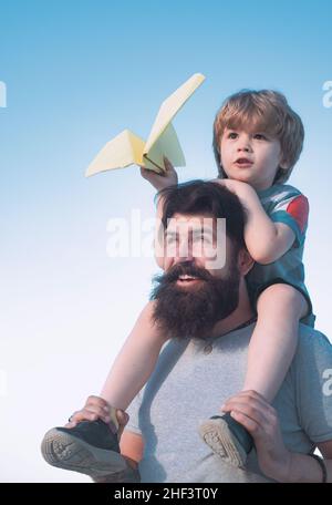 Kinder, die an sonnigen Tagen mit einfachen Papierflugzeugen spielen. Vater gibt Sohn reiten auf zurück im Park. Vater und Sohn spielen - Familienzeit zusammen. Glücklich Stockfoto