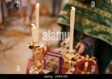 Kerzen brennen auf Kerzenständern vor dem Priester in der Kirche Stockfoto