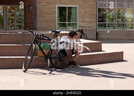 Umea, Norrland Schweden - 10. Juni 2020: Junger Mann mit Kopfhörern und Fahrrad stocht sich am Arm Stockfoto