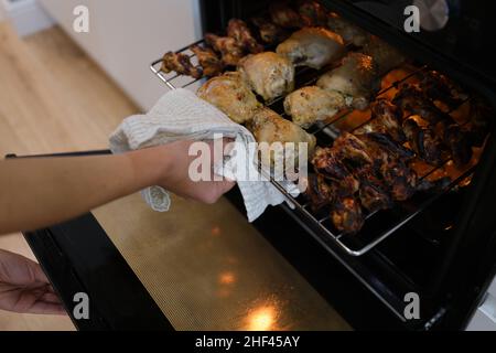 Eine Hand nimmt gebratene Hähnchenflügel und -Beine aus dem Ofen Stockfoto