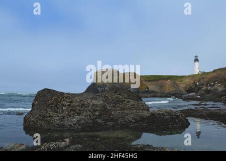 An einem leicht nebligen Tag an der felsigen Küste von Oregon spiegelt sich ein Leuchtturm in einem Tidepool wider Stockfoto