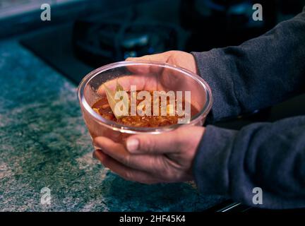 Eine Frau hält eine Schüssel mit Tomatensauce mit Pilzen und Zwiebeln in den Händen Stockfoto