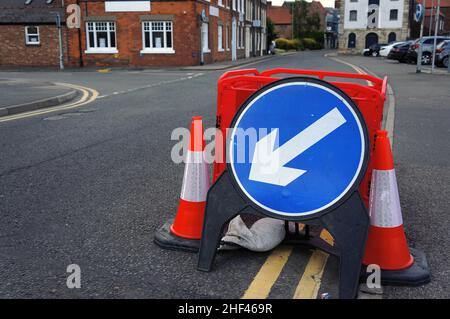 Warnschild mit weißem und blauem Pfeil am Straßenrand mit unschärfem Straßenverlauf im Hintergrund Stockfoto