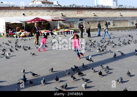 Ein türkisches Mädchen, das auf dem Taksim-Platz in Istanbul, Türkei, zwischen den Tauben läuft und spielt. Stockfoto