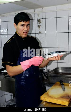 Ein junger türkischer Koch zerteilt Makrelenfischfilets für die beliebten Fisch-Sandwiches in Istanbul, Türkei. Stockfoto