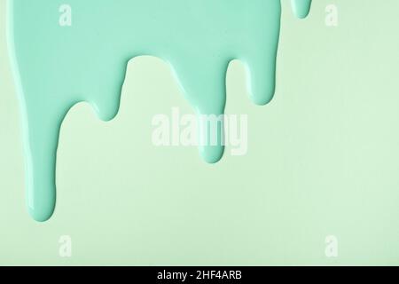 Hellgrüne flüssige Farbtropfen fließen auf olivfarbenem Pastellhintergrund hinunter. Abstrakter cyanfarbener Hintergrund mit Tropfmuster. Acrylmalerei mit Co Stockfoto